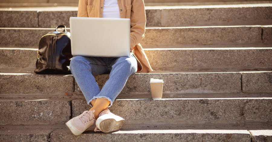 Expats in CEE: a woman sitting on outside stairs and working from her laptop.