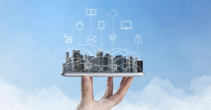 A hand is holding a city with multiple digital service icons on top, layered over a cloudy background.