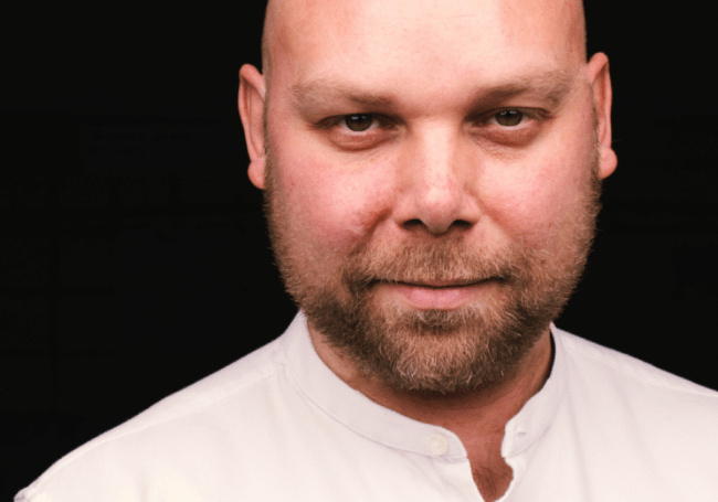 A portrait of Ned Dervenkov, CEO of BESCO wearing a white shirt on a black background