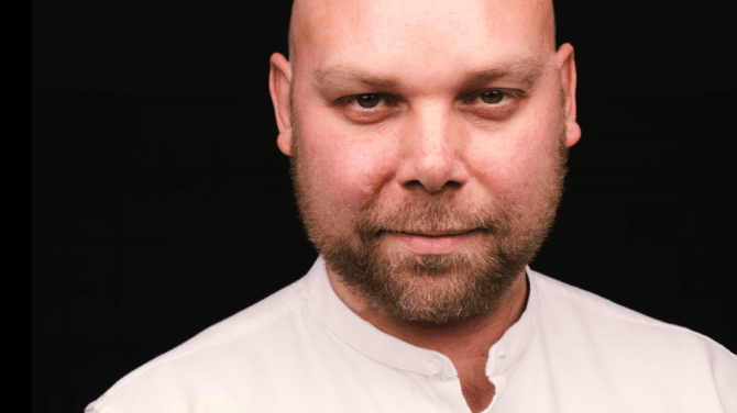 A portrait of Ned Dervenkov, CEO of BESCO wearing a white shirt on a black background